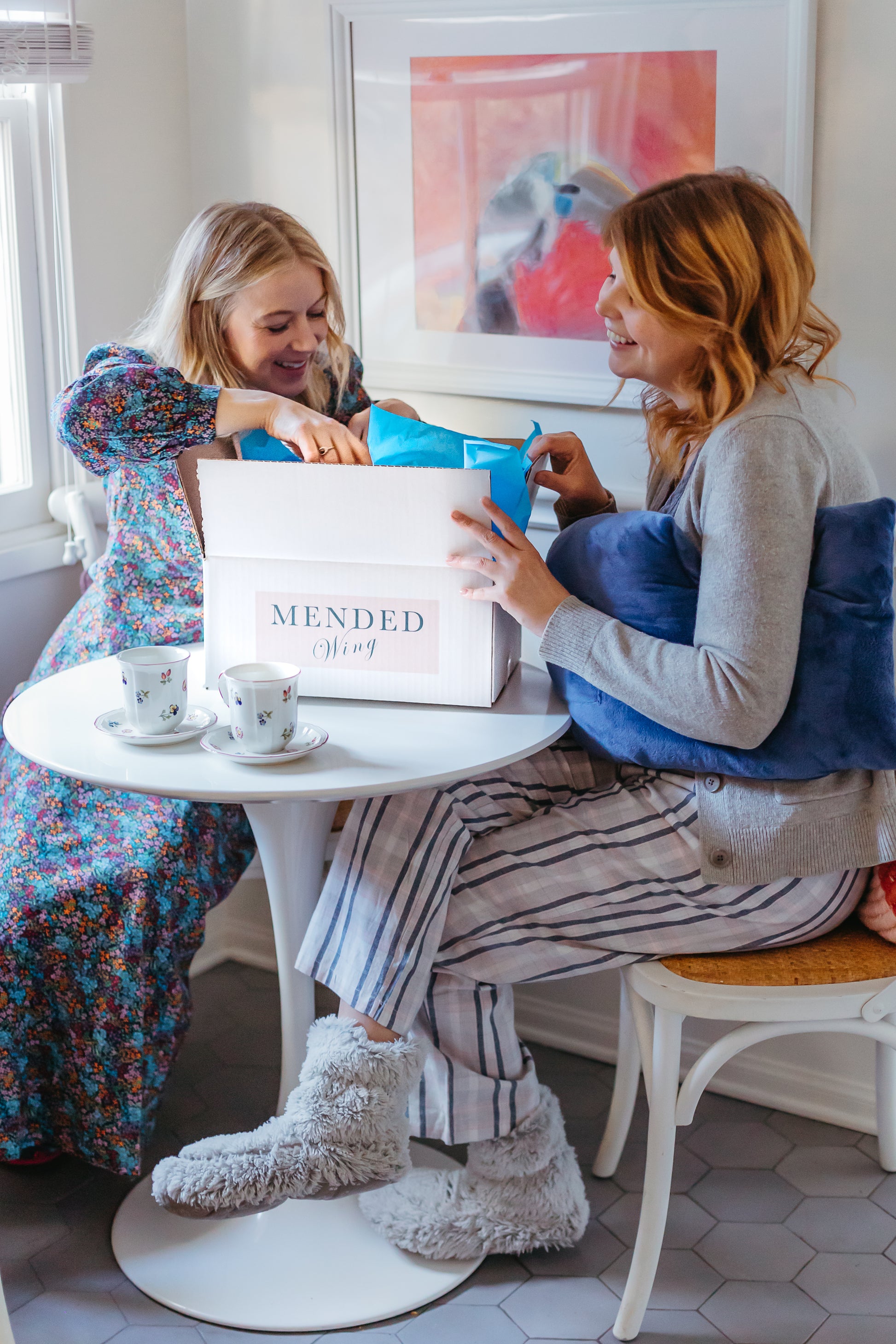 A woman gives her smiling friend a mastectomy recovery bundle to help her recover from her surgery.