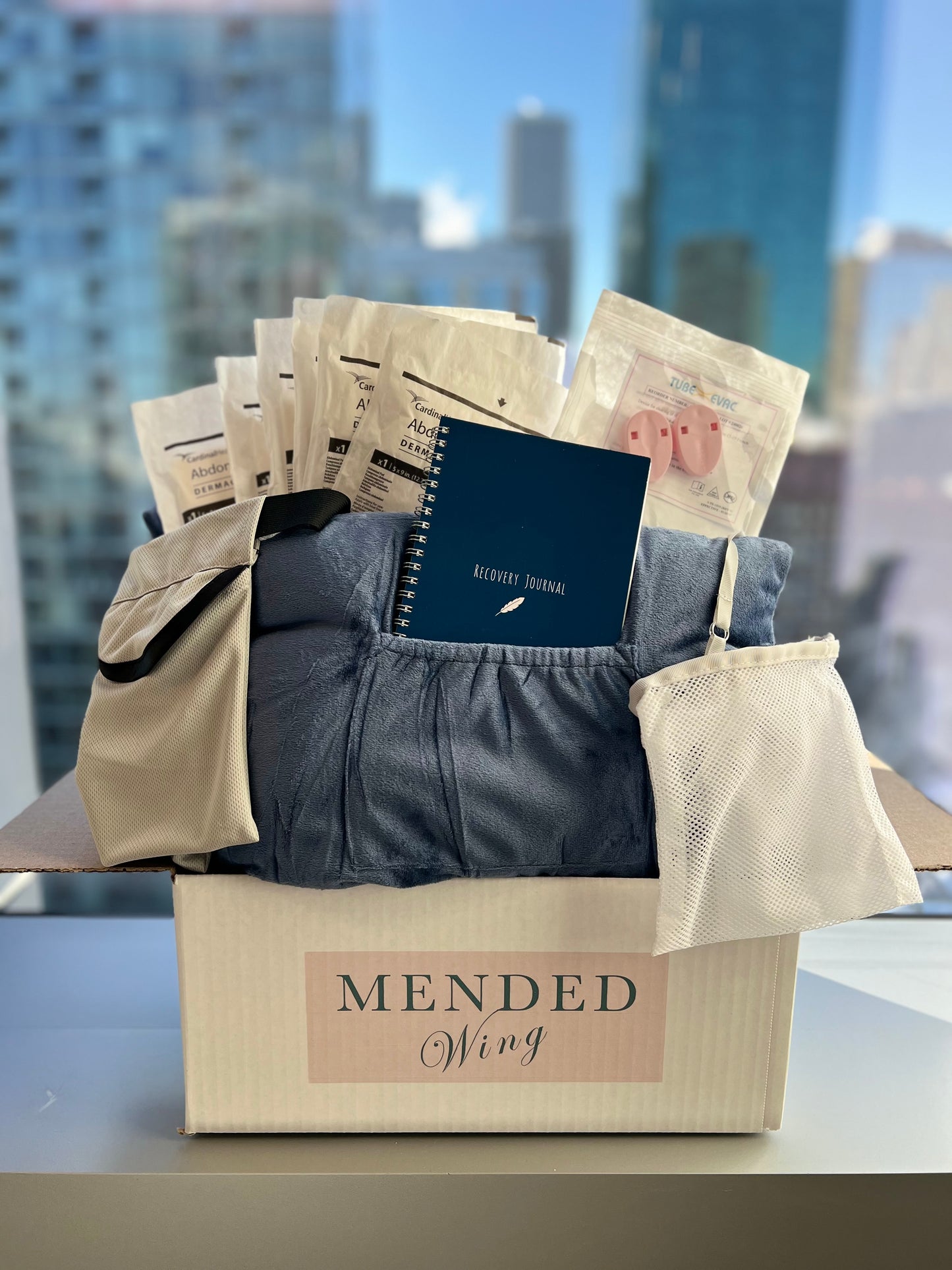 Photo of the Mended Wing recovery bundle featuring a recovery pillow, daily use drain holders, shower drain holders, abdominal pads, and a tube evac.