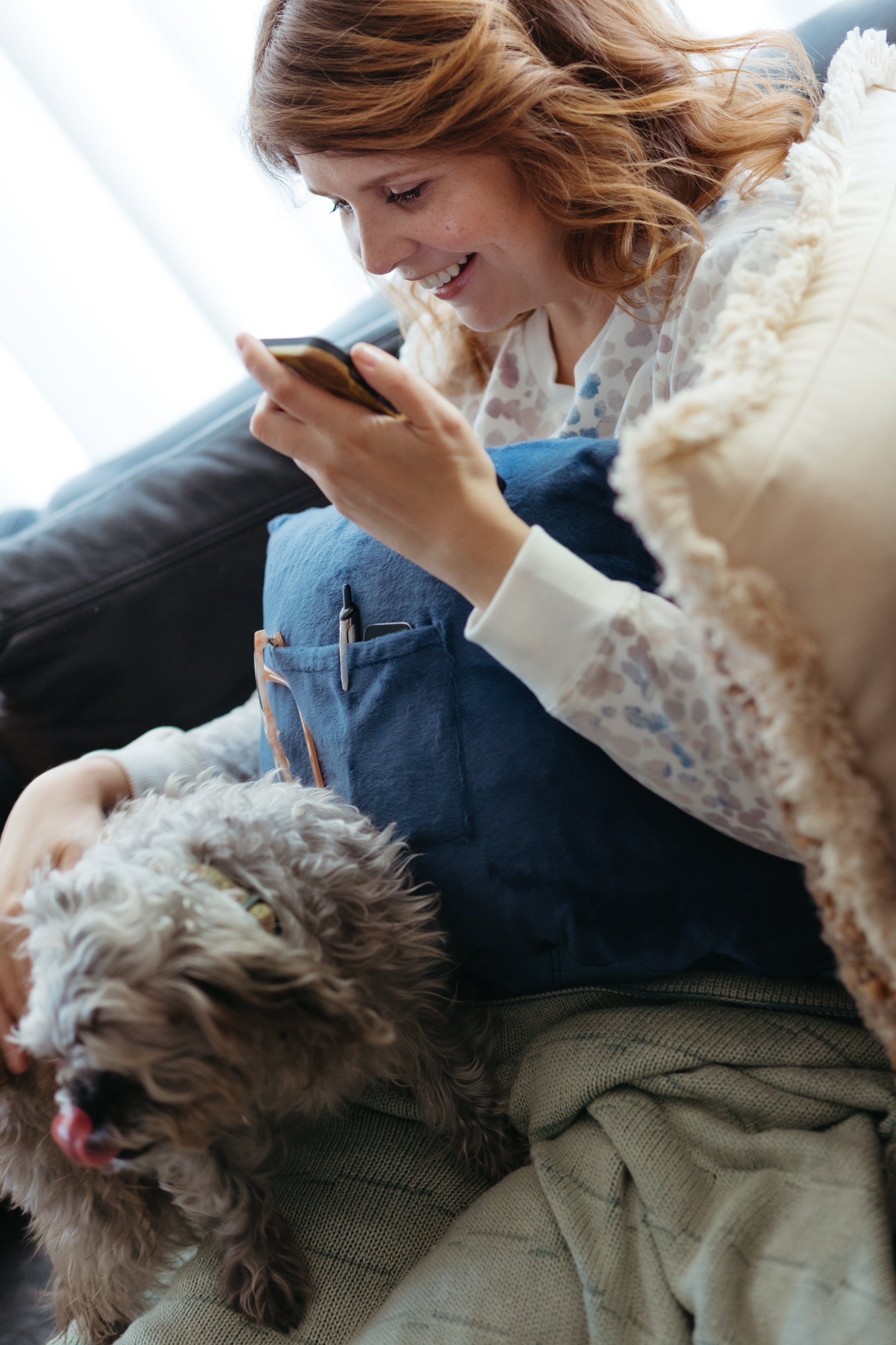 A woman petting her dog while using a breast augmentation recovery pillow.