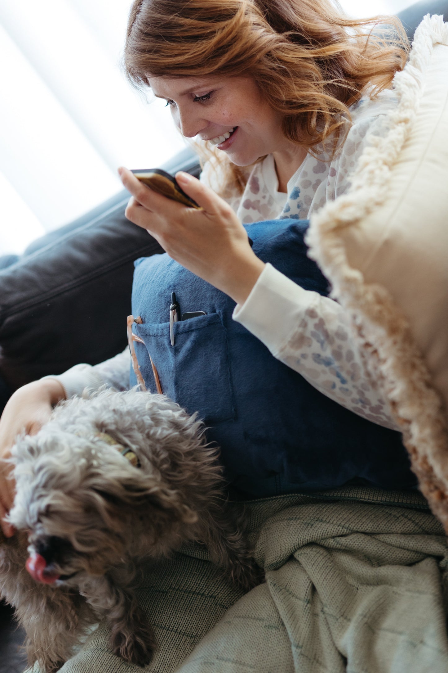 A woman petting her dog while using a breast reduction recovery pillow.