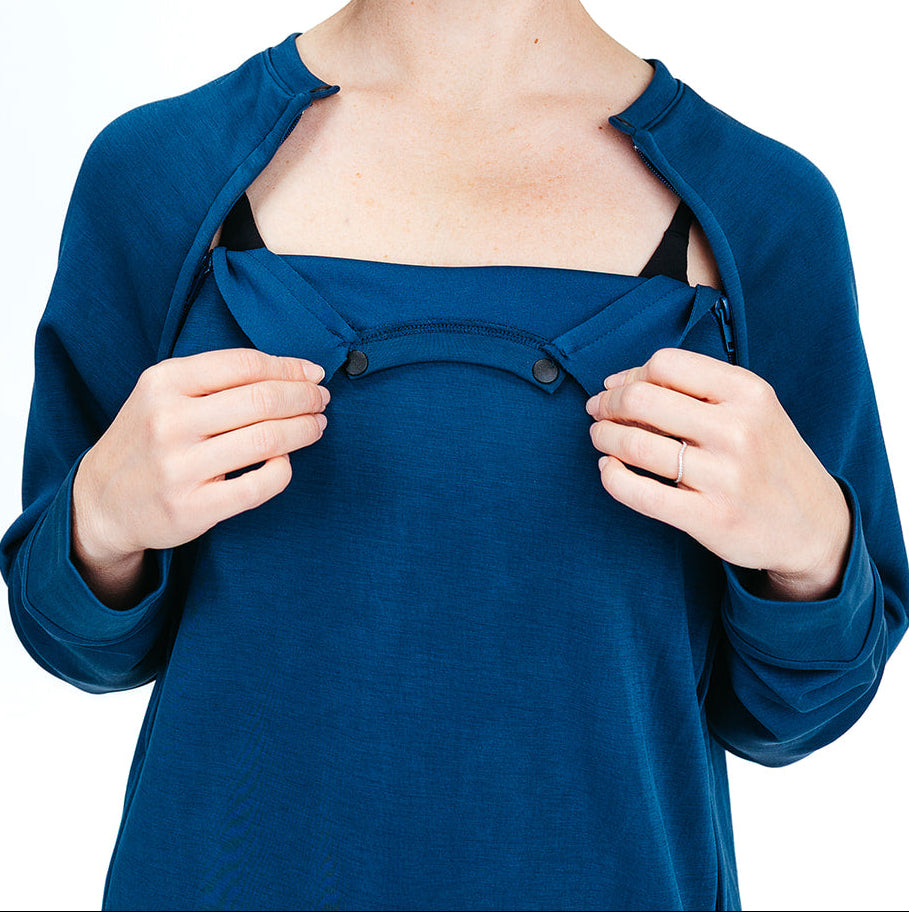 A woman wearing a blue Recovery Crew shirt with the top buttons opened to access surgical sites.