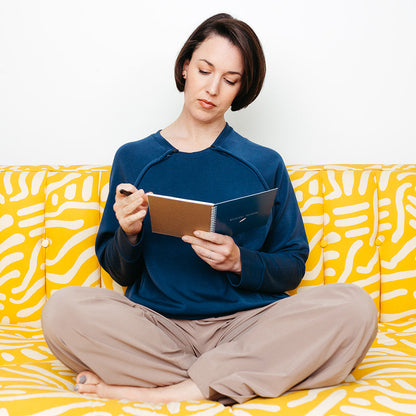A woman writing in the Mended Wing Recovery Journal sitting on a yellow and white patterned couch
