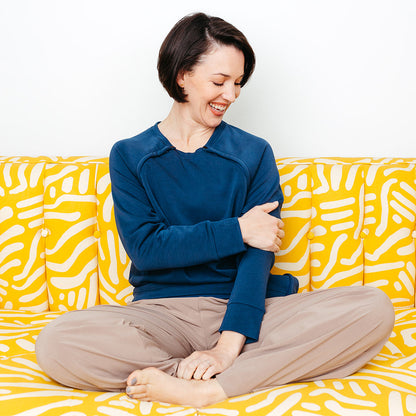 A woman touching the soft fabric of the Mended Wing Recovery Crew sitting on a yellow and white patterned couch