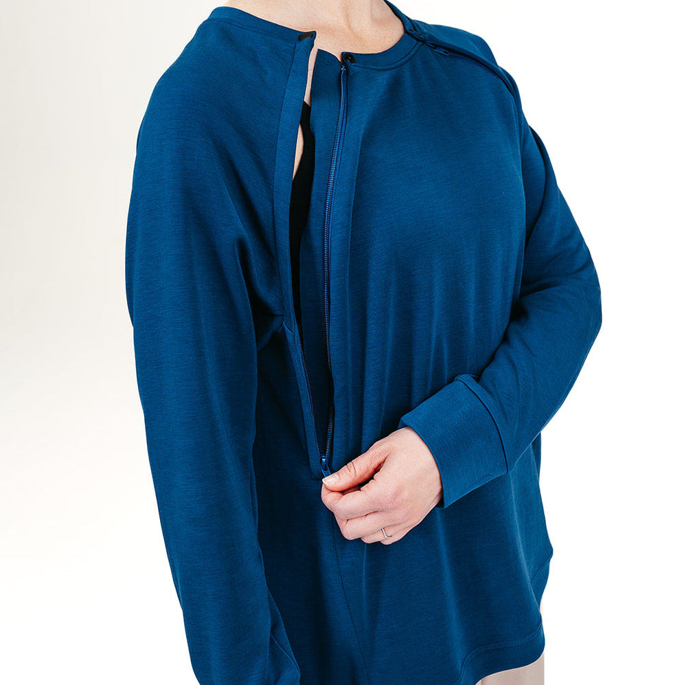 Woman wearing a blue long-sleeve recovery crew on a white background with a side zipper halfway down