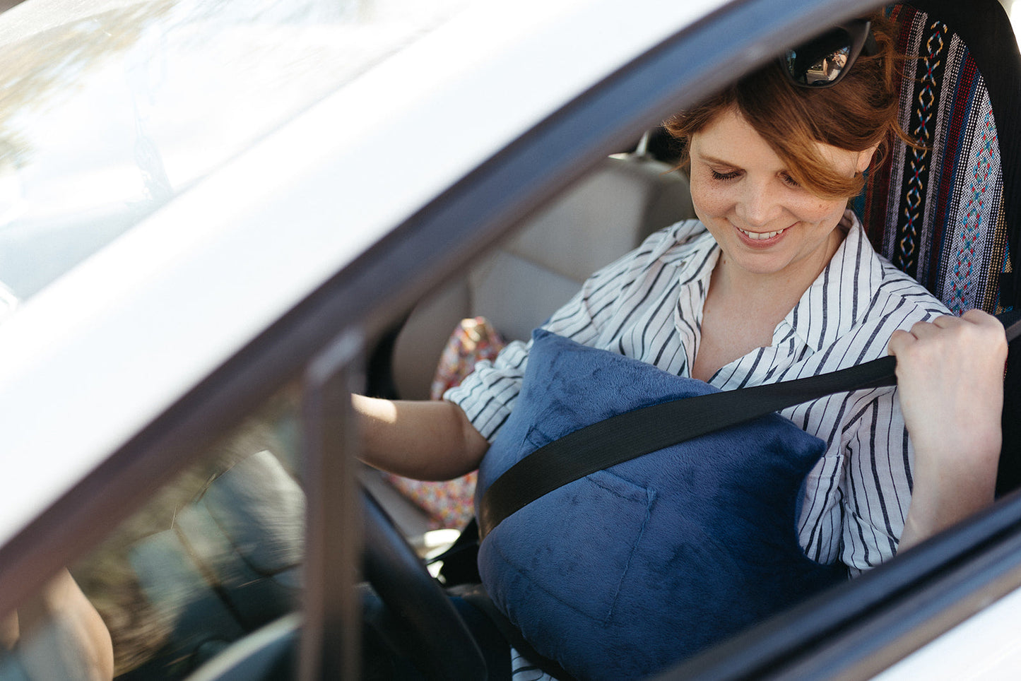 A woman smiling while wearing a seatbelt over her breast augmentation pillow to get back to her daily life after breast augmentation.