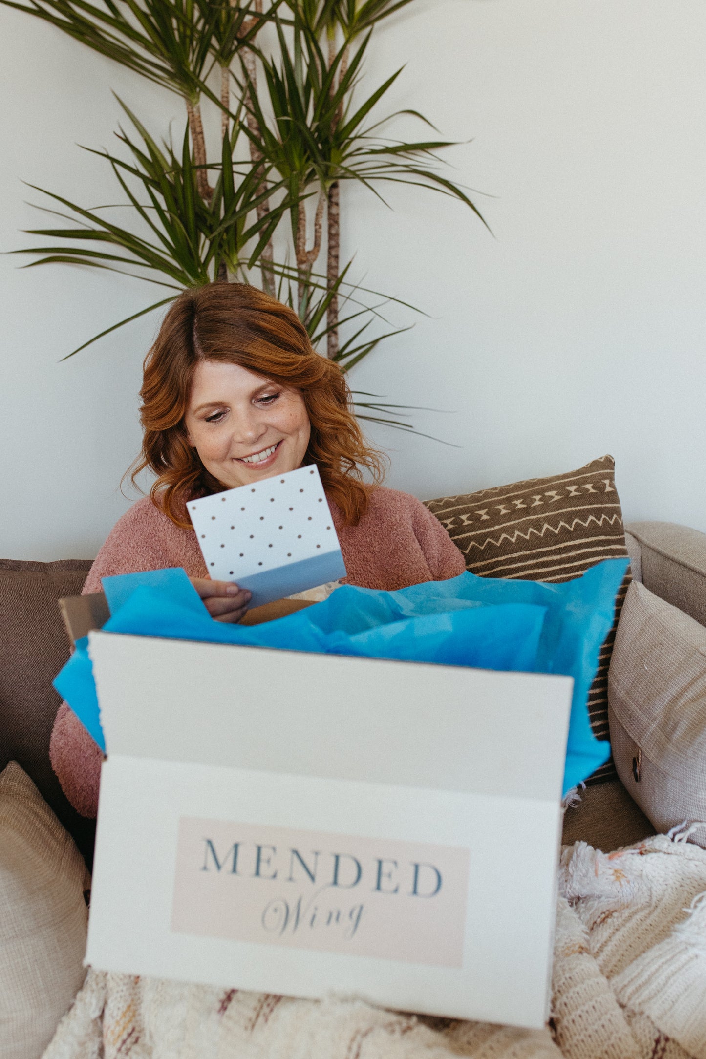 A woman smiling as she reads a note while opening a mastectomy recovery gift bundle.